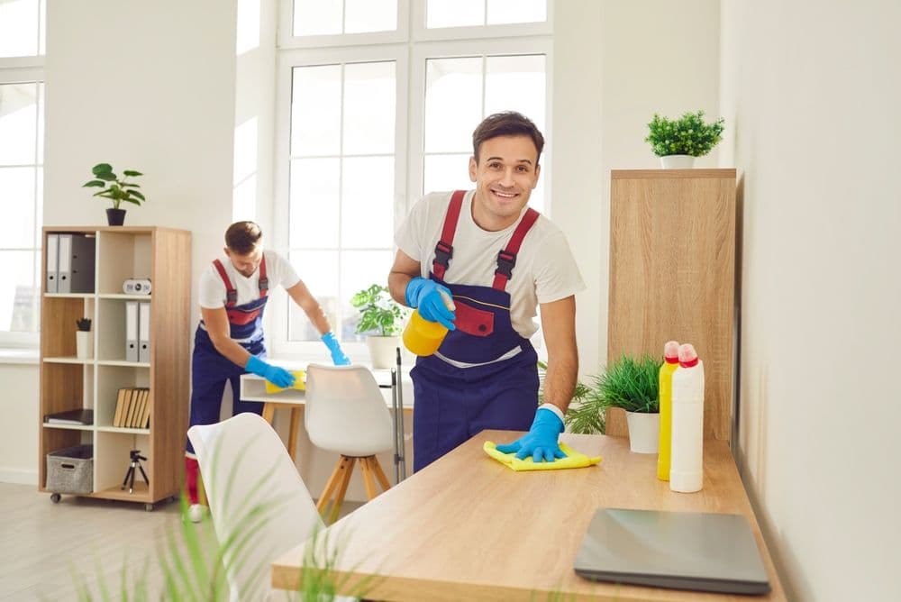 Two cleaners in uniform cleaning a bright office