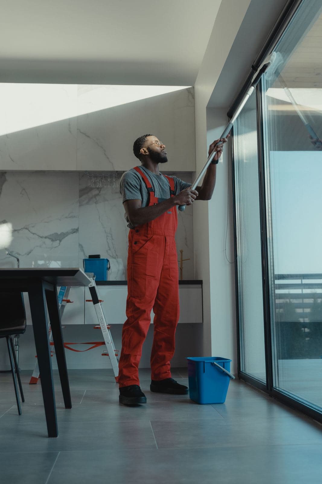 Cleaner washing a large window inside a modern home